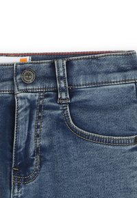 Jeans in denim blu con vita media, cuciture visibili e una tasca frontale. Presentano un bottone in metallo e un'etichetta vicino alla vita.