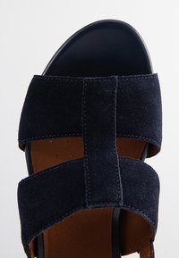 Námořnické modré sukně sandály se širokými pásky, měkkou hnědou stélkou a hladkou černou podrážkou. Design se vyznačuje čistými liniemi a minimálním hardwarem.