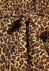 Vestido de tela con estampado de leopardo en colores beige, negro y naranja quemado. Presenta un cinturón atado en la cintura y un acabado suave y texturizado.