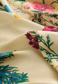 Tela floral con fondo crema, con diseños florales coloridos en rosa, rojo, amarillo y azul, y detalles intrincados de follaje verde.