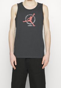 Mörkgrå linne i bomull med en röd och vit Jordan Flight Club-grafik tryckt på framsidan. Ingen ärm, rund halsringning.