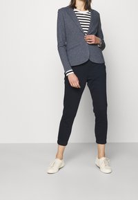 Námořnický blejzr s dvěma předními kapsami, kombinovaný s topem s černobílými pruhy a tmavými kalhotami, doplněný béžovými teniskami.