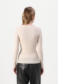 Beige ribbet langermet topp med rund hals, kombinert med svarte skinnbukser som har en tett passform og strukturert stoff.