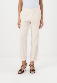 Pantaloni beige chiaro con vita elastica e orli arrotolati, realizzati in un tessuto morbido. Abbinati a sandali neri con tacco alto e cinturini.