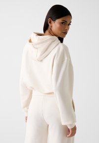 Hoodie in crèmekleur met een losse pasvorm, voorzien van een geribbelde zoom en manchetten, en een voorzak. Zachte textuur, minimalistisch ontwerp.