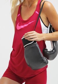 Rode mouwloze sporttop met roze Nike-logo, gecombineerd met zwarte bokshandschoenen. De stof lijkt lichtgewicht en ademend.