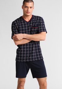 Marineblauw geruit pyjama set met een V-hals korte mouwen top met een zak en effen korte broek. Inclusief rode accenten in het ontwerp.