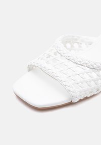 White open-toe sandal with woven leather straps and a square toe design on a light background.