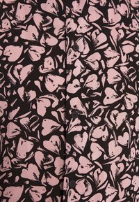 Knappblus med svart bakgrund och ett mönster av rosa hjärtan. Materialet är slätt med en mjuk textur; inkluderar svarta knappar.