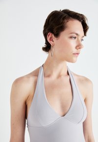 Šedý plavky s halter krkem a hlubokým výstřihem, bezšvový design a hladká textura. Výrazný díky svému minimalistickému stylu a čistým liniím.