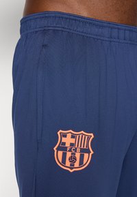 Marineblå sportshorts med et broderet orange FC Barcelona-våbenskjold. Materialet er glat, med en elastisk talje og sidelommer.