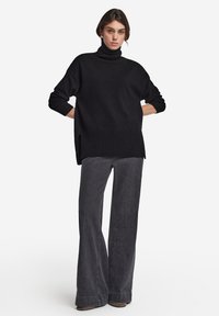 Sort rullekrave sweater med ribbet kant, parret med brede grå bukser med en subtil tekstur og en afslappet pasform.