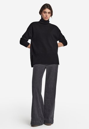 Maglione nero a collo alto con orlo a costine, abbinato a pantaloni grigi a gamba larga caratterizzati da una trama sottile e una vestibilità rilassata.