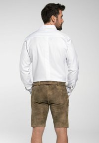 Camisa blanca de botones con mangas largas, combinada con pantalones cortos de ante marrón claro que tienen un bolsillo lateral y detalle de botón en la parte trasera.