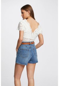 Crop top en dentelle blanche avec des manches courtes et un dos en V profond, associé à un short en denim bleu. Le short a des poches arrière et un ourlet effiloché.
