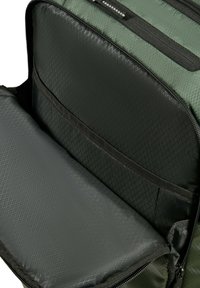 Groene rugzak met een gestructureerd buitenmateriaal, voorzien van een groot hoofdcompartiment en een kleinere, met rits afsluitbare zak. De binnenkant heeft een ruitpatroon.