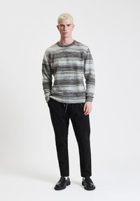 Strickpullover mit grauen und weißen horizontalen Streifen, rundem Ausschnitt und gerippten Bündchen, kombiniert mit schwarzen Hosen und schwarzen Schuhen.