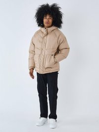 Beige pufferjakke med hætte, med knaplukninger og to frontlommer. Båret med sorte cargo-bukser og hvide sneakers.