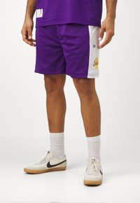 Pantaloni corti da basket viola realizzati in tessuto a rete, con pannelli laterali bianchi, logo dei Lakers e una vestibilità comoda. Indossati con calze bianche e sneaker.
