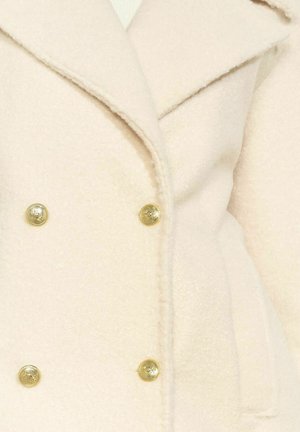 Doppelreihiger Mantel aus weichem, hellbeigem Stoff mit goldfarbenen Knöpfen und Reverskragen. Die Textur wirkt flauschig und warm.