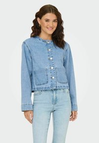 Veste en denim bleu clair avec un col rond, fermeture à boutons et deux poches avant. Manches longues et coupe courte pour une silhouette moderne.