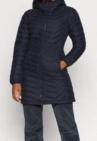 Marinblå pufferjacka med huva, med en chevron-kviltad design och frontdragkedja. Inkluderar sidofickor och åtsittande ärmavslut.