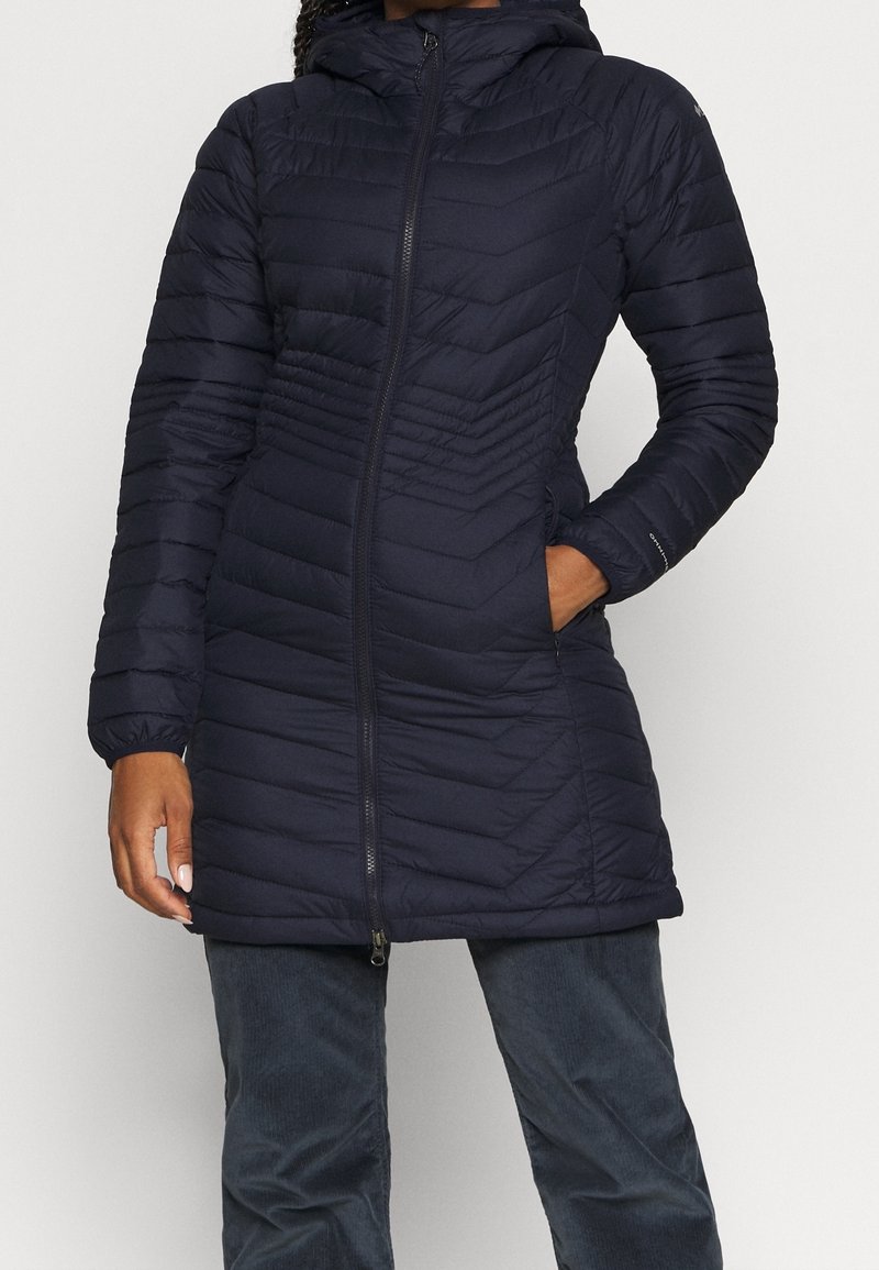 Marinblå pufferjacka med huva, med en chevron-kviltad design och frontdragkedja. Inkluderar sidofickor och åtsittande ärmavslut.