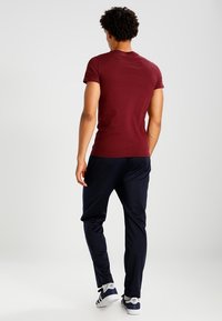 Camiseta ajustada color burdeos de manga corta combinada con pantalones jogger oscuros de color marino. El modelo lleva zapatillas informales blancas con rayas negras.