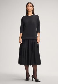 Czarny, długi rękaw top połączony z plisowaną czarną spódnicą. Zestaw wyróżnia się gładką tkaniną i eleganckim fasonem, dopełnionym lakierowanymi obcasami.