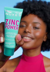 Grön tub med Nuxe Zinc Power, med rosa text, har en matt finish och ett flip-top lock. Texten inkluderar produktinformation. Storlek: 40 ml.