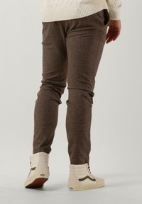 Brown textured slim-fit pants with side pockets, paired with white high-top sneakers featuring green accents.