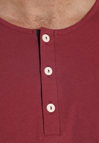 Burgundy henley shirt with a rounded neckline, features three cream-colored buttons down the front, made of soft, stretchy fabric.