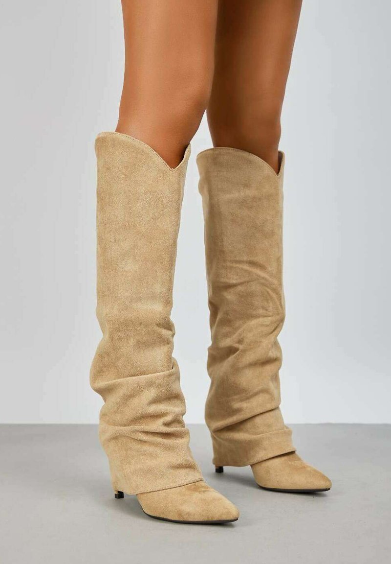 Bottes slouch à hauteur de genou en suède beige, avec des orteils pointus et un design enveloppant, offrant une texture douce et un talon aiguille.