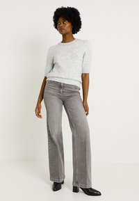 Suéter gris claro texturizado de manga corta y cuello redondo, combinado con pantalones gris de tiro alto y botas de tacón negras.