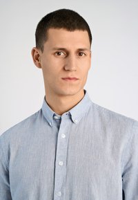 Camicia button-up azzurro chiaro realizzata in tessuto testurizzato, con colletto e bottoni bianchi. Cuciture visibili lungo le cuciture.