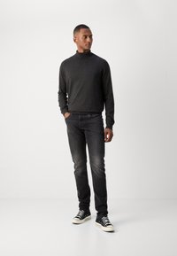 Pull à col roulé gris foncé, jeans slim fit noirs, et sneakers noires avec semelles blanches. Texture lisse, apparence décontractée, détails minimalistes.