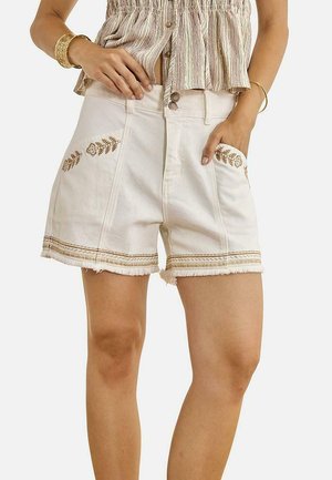 Mujer con shorts blancos de cintura alta con bolsillos bordados y bajos deshilachados, combinados con una camiseta de rayas sin mangas y pulseras doradas.