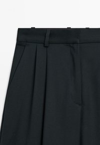 Black tailored trousers featuring a flat waistband, front pleats, and a side pocket detail, made from a smooth, matte fabric.