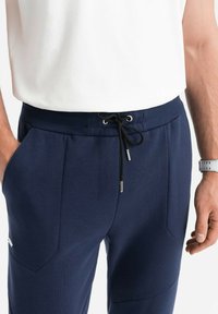 Navy blauwe joggerbroeken van zachte stof met een trekkoord in de taille en metalen tips, voorzakken en een slanke, op maat gemaakte pasvorm.