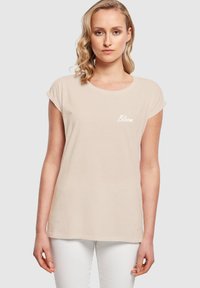 Beige puuvillane T-särk lühikeste rulli varrukatega, ümar kaelus ja ees valge "Bloom" tekst. Kandsid valgeid pükse.