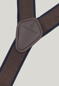 Brązowe materiałowe szelki z granatowymi krawędziami, z skórzaną łatą z wytłoczonym napisem "PRÓCHNIK". Teksturowana, solidna konstrukcja odpowiednia do formalnych strojów.