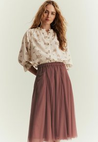 Krämfärgad blus med blommönster och volangkrage, kombinerad med en transparent lila tullekjol med elastisk midja.