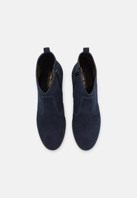 Botines de ante azul marino con una textura suave, que cuentan con cremalleras laterales y paneles elásticos para poner y quitar fácilmente, diseñados con una puntera redondeada.