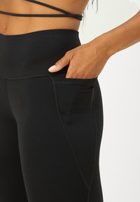 Magas derekú fekete leggings sima anyagból, oldalsó zsebe van, varrás nélküli kialakítással és karcsú szabású lábszárakkal.