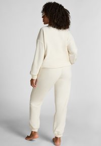 Crèmekleurige loungewear set gemaakt van zachte, textuurstof. De top heeft een relaxte pasvorm, terwijl de broek elastische manchetten en een elastische tailleband heeft.