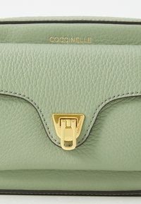 Borsa a tracolla verde in pelle con finitura testurizzata, chiusura in metallo dorato e bordi a contrasto. Logo stampato in oro sulla parte frontale.