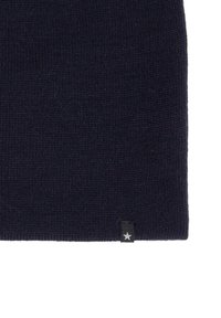 Tamsiai mėlynas megztas beanie, pagamintas iš minkštos vilnos, su raunamu paviršiumi. Yra mažas juodas etiketas su baltu žvaigždžių akcentu.