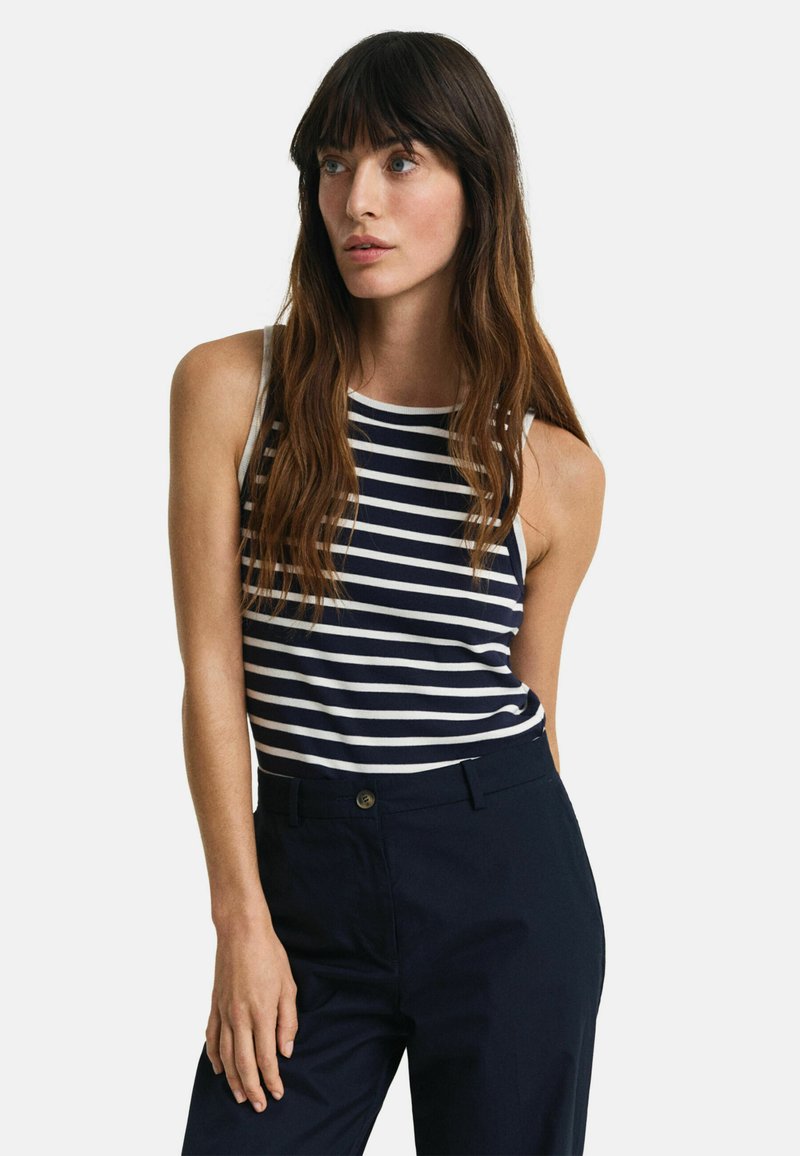 Stribet tanktop i marineblå og hvid, med et tætsiddende design og brede stropper, parret med mørke bukser. Glat bomuldsstof.