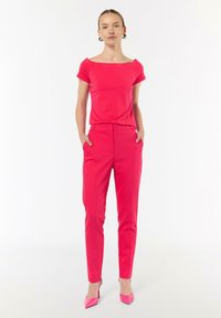 Różowa dopasowana bluzka z dekoltem odsłaniającym ramiona, w połączeniu z dopasowanymi różowymi spodniami. Różowe szpilki dopełniają stroju.