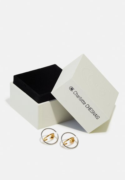 Gold- und Silberohrringe in runder Form in einer weißen Box mit einem schwarzen Samtfutter. Die Box verfügt über ein Logo auf der Vorderseite.